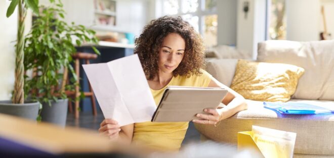 Woman holding paper looking at tablet