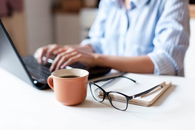Person working on laptop with coffee and glasses